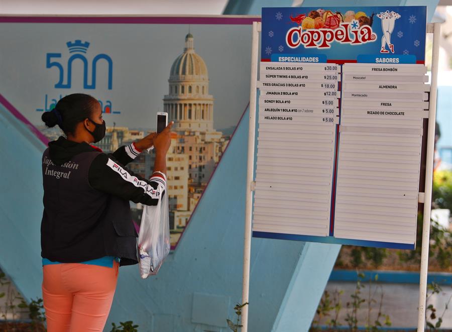 Una mujer toma fotos a un tablero con los precios de la heladería Coppelia